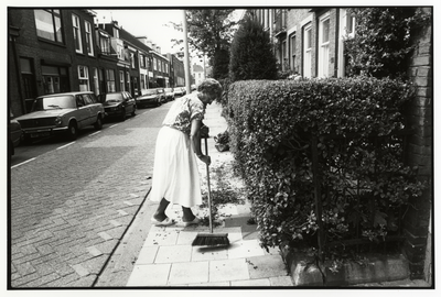 108006 Afbeelding van een dame die de stoep veegt, na het knippen van de heg, bij het huis Bekkerstraat 58 te Utrecht.